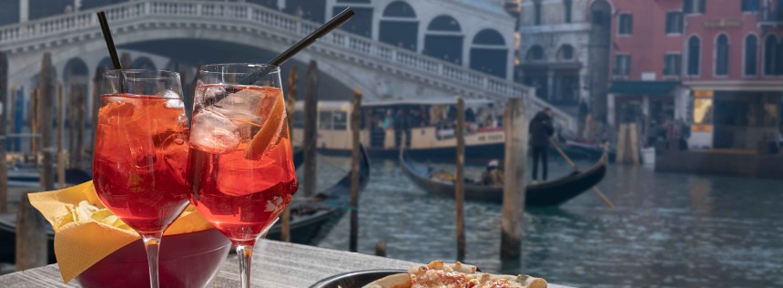 Cocktail for two prepared with straws and lemon and a bowl of snacks. In the background the Rialto Bridge in Venice.