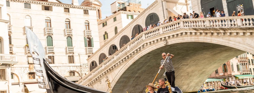 The famous buildings and Rialto bridge of the old city of Venezia along the grand canal river with a gondola passing.